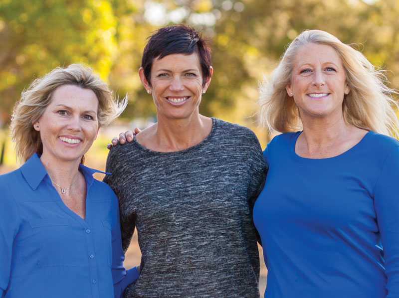 Three lady friends smiling outside.